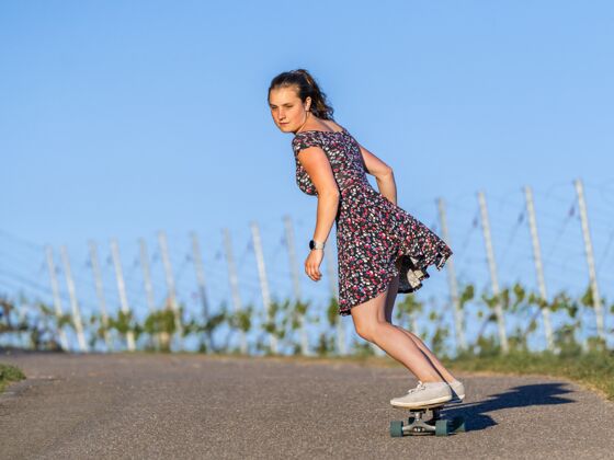 运动年轻女子在绿树环绕的空旷路上滑滑板运动休闲活动