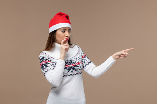 视图正面图：年轻女性戴着红帽子在深棕色背景上摆姿势 感慨圣诞新年女性情感姿势