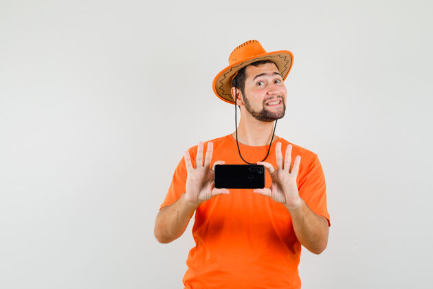 男性年轻人穿着橘色t恤 戴着帽子在手机上拍照 看上去兴高采烈 眼前一亮男人成人人