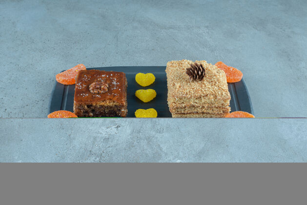 美味在大理石表面的海军蓝板上放一块蛋糕 烤面包和一些果冻糖果蛋糕美味甜点