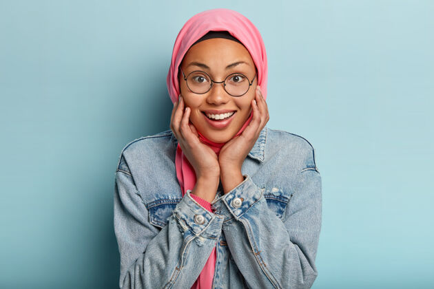女性美丽快乐的阿拉伯女性轻轻抚摸脸颊 拥有迷人的笑容 头上戴着传统的粉色面纱皮肤健康情绪