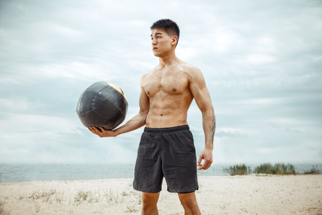 人年轻健康的男子运动员在海滩上做深蹲男性强壮年轻