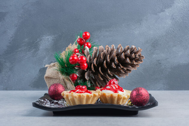 沙司把草莓酱纸杯蛋糕放在一个黑色的盘子里 在大理石表面绑上圣诞装饰品草莓美味圣诞节