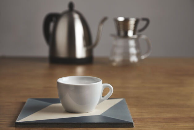 咖啡师白色空白咖啡杯前现代茶壶和美丽的透明滴咖啡机在咖啡厅的厚木桌上放着陶瓷盘子上的杯子厨房热的咖啡馆