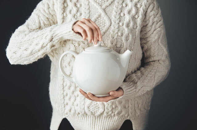 味道穿着暖和毛衣的女人拿着一个大的白色茶壶 茶壶的形状是心形的正视图 一张破旧的木桌安法斯 没有脸心犹太季节