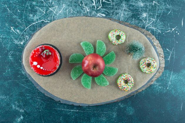 蛋糕树雕像 蛋糕 marmelades 甜甜圈和一个苹果在蓝色的木板上视图雕像水果