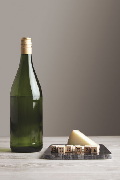 牛奶绿色葡萄酒果汁瓶靠近大理石板 上面有木制字母“奶酪”和“山羊奶酪” 隔离在白色空白的背面和桌子上大理石果汁葡萄酒