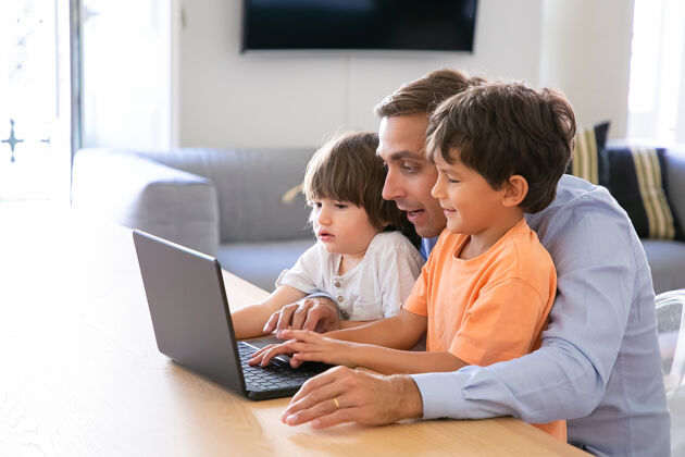 白种人出柜的父亲向小儿子展示笔记本电脑上的东西可爱的高加索男孩在家里学习电脑 在慈爱的中年父亲的帮助下父亲 童年和数字技术的概念沙发爱父亲