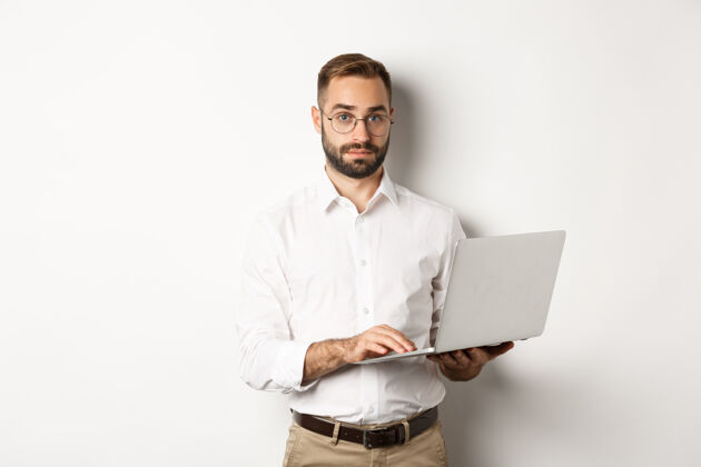 成年人做生意年轻英俊的商人在笔记本电脑上工作 在电脑上工作 站着时髦笔记本电脑手势
