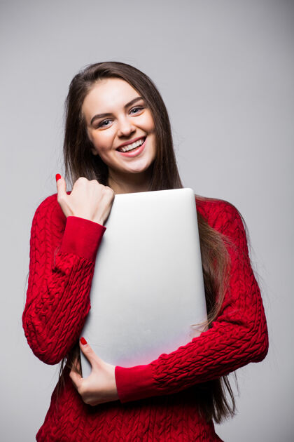 年轻年轻女子站着拿着笔记本电脑快乐的年轻女孩在用她的笔记本电脑 隔离在白色的墙上休闲微笑漂亮