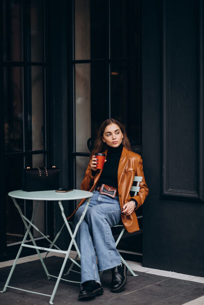 女性坐在咖啡馆外面喝咖啡的年轻女孩快乐女人快乐夹克