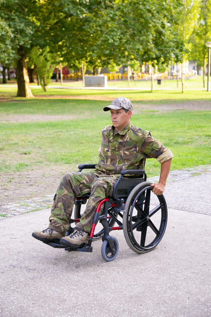 受伤残疾军人在轮椅上穿着迷彩服 沿着城市公园的步道前行退伍军人还是残疾概念退休草成人