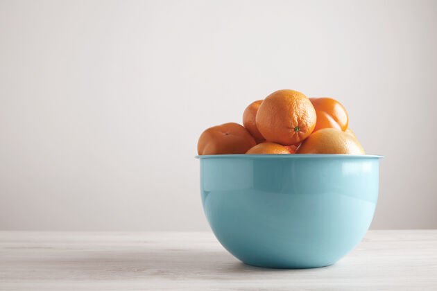 水果不同的水果和柑橘放在蓝色金属大碗里 放在白色木桌边的空白墙上柑桔葡萄柚碗
