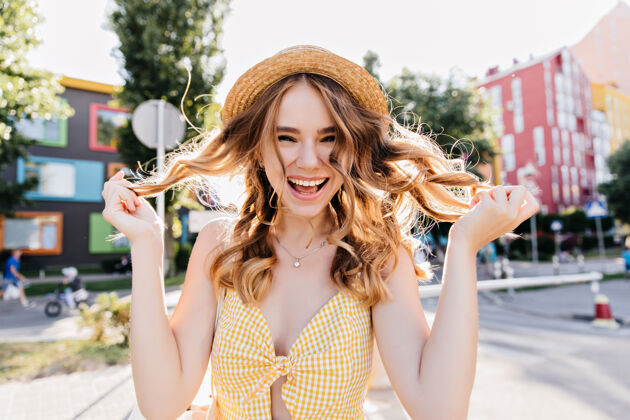 Fun迷人的欢笑女人玩着她的波浪形金发穿着黄色连衣裙和复古帽子的可爱女孩的户外照片TownPlayfulHat