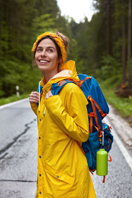 人类笑容可掬的欧洲女青年头戴黄色头带 身穿雨衣 背着背包乐观自由背包客