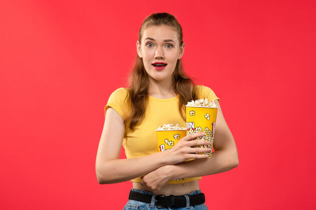 电影正面图年轻的女性在电影院拿着爆米花在红墙电影院的女性色彩电影院色彩爆米花