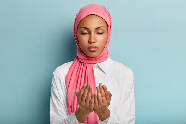 东方阿拉伯忠实的黑皮肤女子双手祈祷 祈求身体健康 信奉健康有面纱的头 穿着白衬衫闭着眼睛享受宁静的气氛祈祷信仰展示