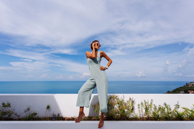 年轻在豪华别墅的teracce阳台上 穿着浅蓝色薄荷色的棕褐色高加索女人 可以欣赏到迷人的热带海景风景完美海