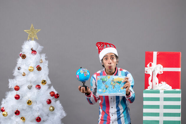 圣诞老人前视图惊讶的男子与螺旋弹簧圣诞帽举行世界地图和地球仪举行快乐惊喜的人