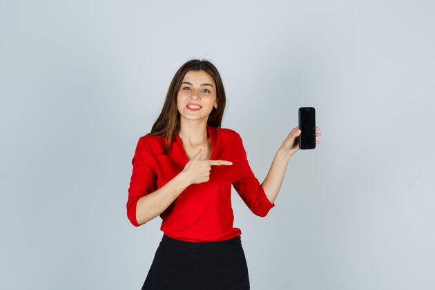 手机年轻的女士指着手机 穿着红色的衬衫 裙子 看起来很高兴享受青春女性