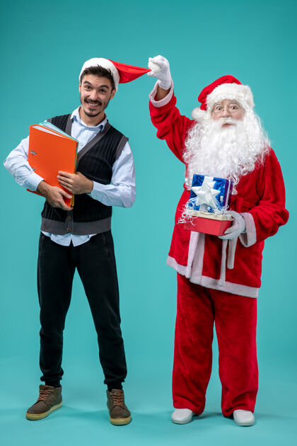 圣诞快乐圣诞老人与年轻男性和礼物在蓝色墙上的正面视图圣诞老人年轻人男人