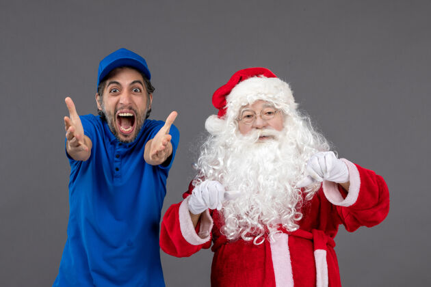 十二月灰色墙上的圣诞老人和男信使的正面图人们圣诞老人节日