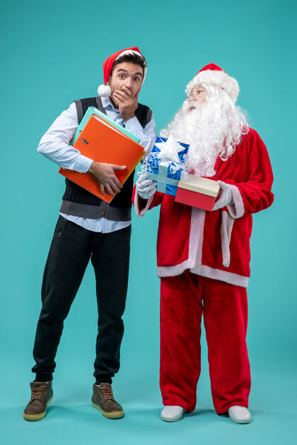 时尚圣诞老人与年轻男性和礼物在蓝色墙上的正面视图年轻寒冷圣诞老人