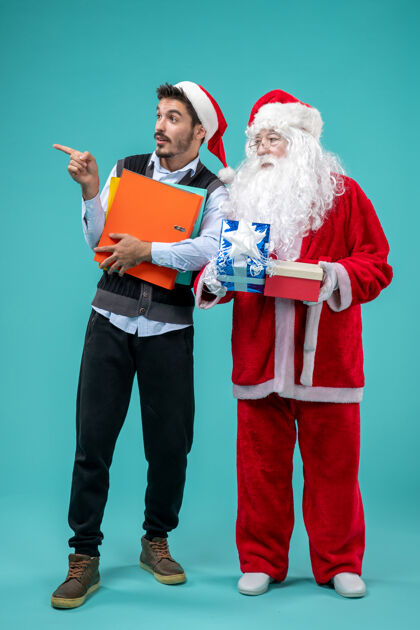 快乐圣诞老人与年轻男性和礼物在蓝色墙上的正面视图人们音乐家圣诞快乐