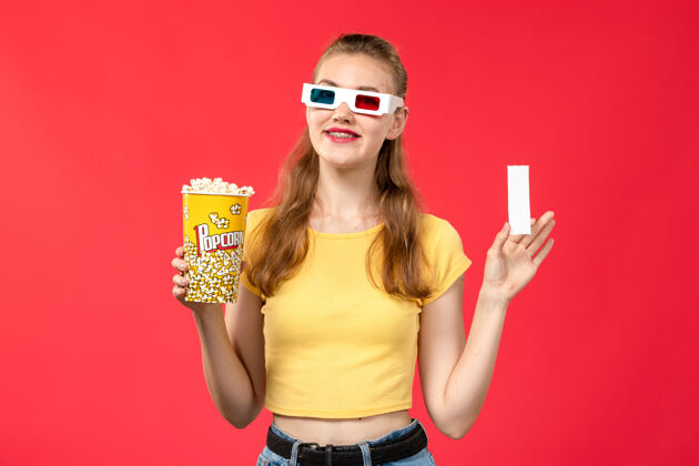年轻人正面图年轻女子在电影院拿着爆米花包和红墙电影院的电影票女孩观点肖像电影