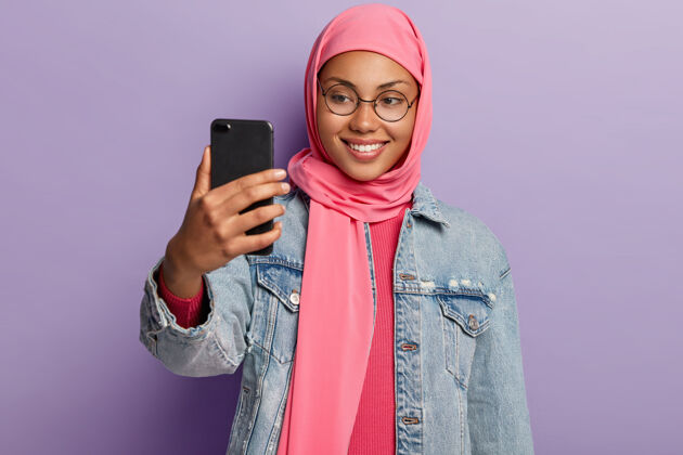 手机表情开朗的阿拉伯年轻女子 戴着圆眼镜 通过手机打视频电话高兴高兴设备