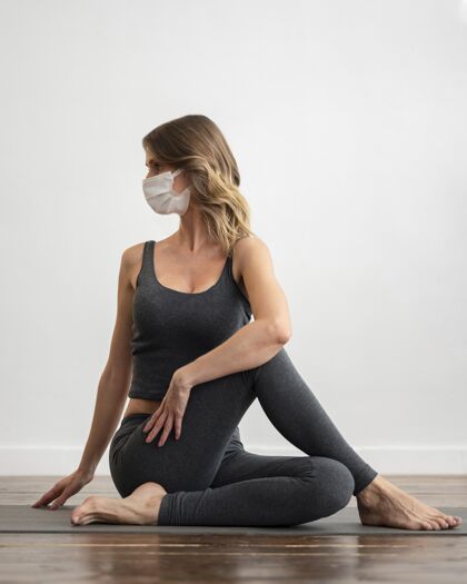 垂直戴着医用面罩的女士在家做瑜伽的正面图休闲冥想反省
