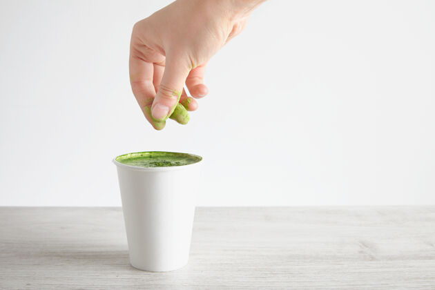 饮料女人的手把绿色有机优质抹茶粉倒在抹茶拿铁咖啡上 放在木桌上 白色的背景表面玻璃牛奶