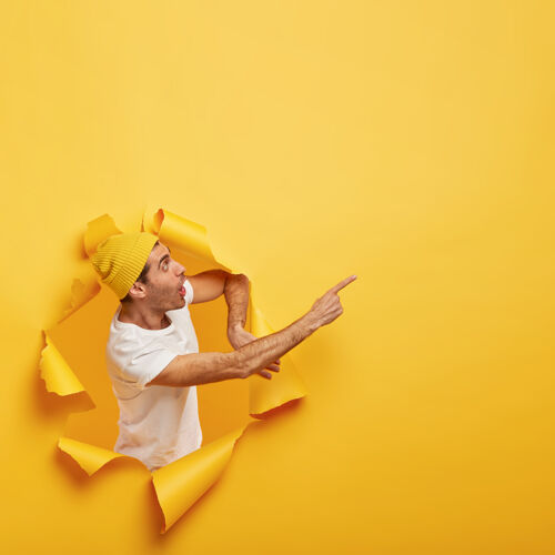 促销情感惊讶的家伙站在纸洞与撕破的黄色边缘 显示难以置信的复制空间反应旁边开放