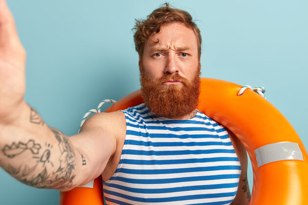 休闲严肃愤怒的红头发浓密胡须的男人自拍肖像 戴着救生圈安全水手冒险