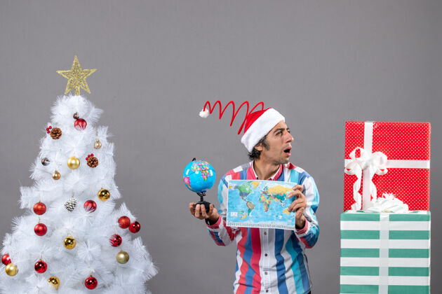 家伙前视图撬动人与螺旋弹簧圣诞帽看礼物持有世界地图和地球仪假期圣诞老人人