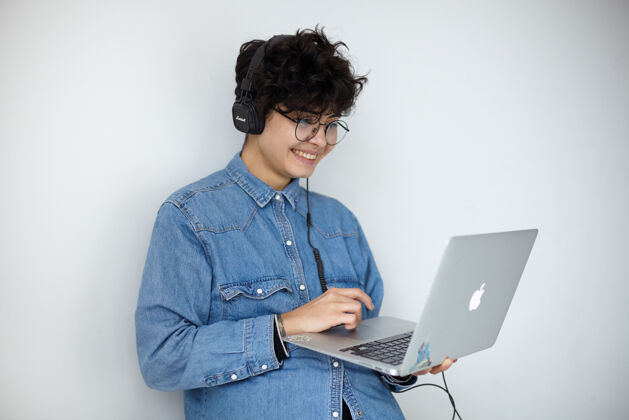 短发年轻可爱的正面卷发黑发女士 短发时髦 手持笔记本电脑 手放在键盘上 一边愉快地看着屏幕上令人愉快的视频工作年轻人凸起