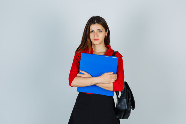 现代年轻的女士背着红色上衣的背包 裙子夹着文件夹 看上去很严肃愤怒人休闲