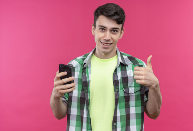 电话微笑的白人年轻人穿着绿色衬衫 在孤立的粉色背景上举着大拇指向上粉色微笑