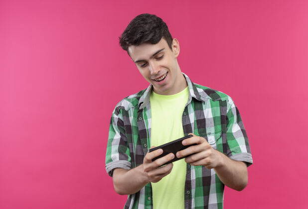 穿着微笑的白人年轻人穿着绿色衬衫 在孤立的粉红色背景下打电话玩游戏绿色电话粉色