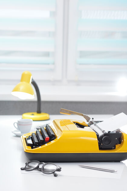 记者靠窗的白色办公桌上有一台黄色打字机 上面有台灯和咖啡新闻写作窗户