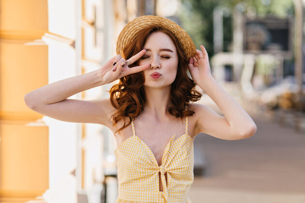 明亮可爱的姜黄色连衣裙女孩在城市里摆出亲吻的表情美丽的卷发女士戴着时髦的草帽享受夏日周末姜休闲红发
