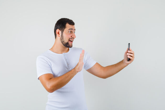站立一个年轻人穿着白色t恤 一边打视频电话一边打招呼 看上去很开心休闲男人肖像