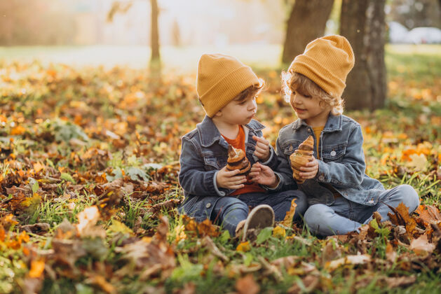 糕点两个男孩兄弟坐在公园的草地上吃羊角面包秋天卷曲孩子