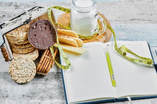 面包房木桌上放着一篮饼干和一罐牛奶 还有一本笔记本烹饪燕麦片堆