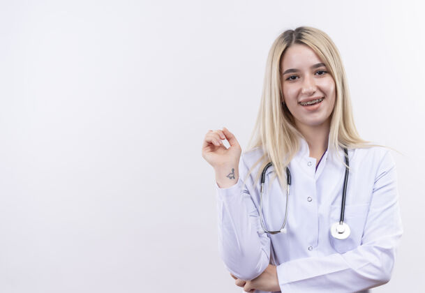 医疗微笑的医生年轻的金发女孩戴着听诊器和医用长袍戴着牙套在孤立的白色背景医生牙科听诊器