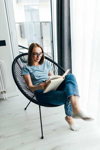 现代年轻的懒女人在家里坐在窗前的现代椅子上 在客厅里放松看书休闲酒店美丽