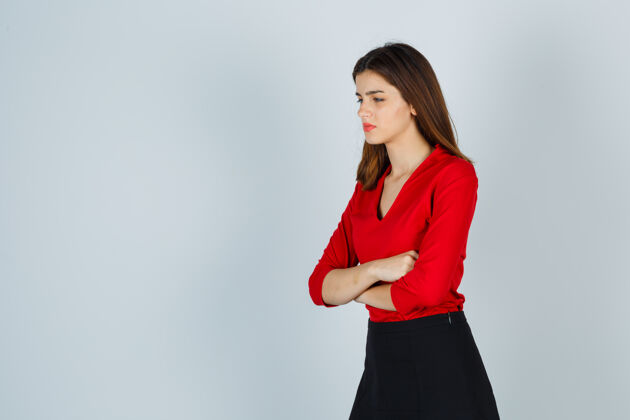 办公室年轻的女士交叉着双臂站在那里 穿着红色的衬衫望着别处人手臂女人