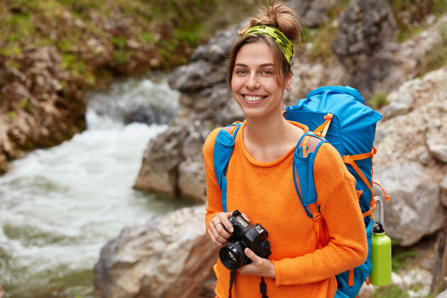 高兴积极的年轻旅行者带着相机和背包对着峡谷摆姿势 享受大自然和风景冒险休息摄影师