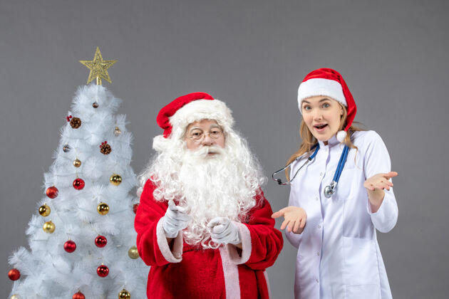 年轻圣诞老人和年轻女医生在灰色墙上的正视图男性节日圣诞快乐