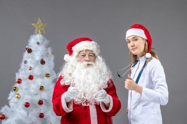 庆祝圣诞老人和年轻女医生在灰色墙上的正视图圣诞老人女性圣诞快乐